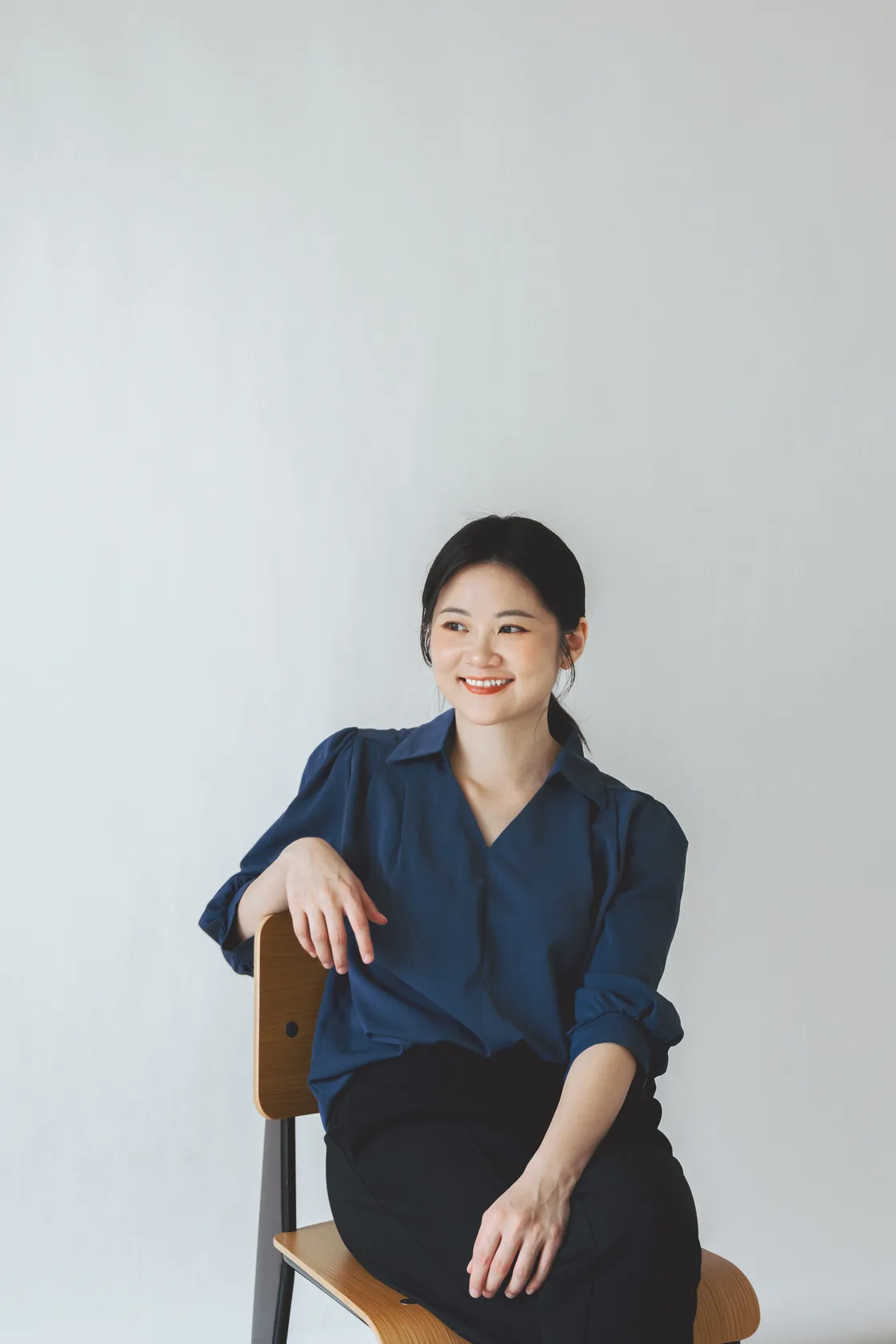 Lauren 穿著深藍襯衫，坐在木椅上自然微笑