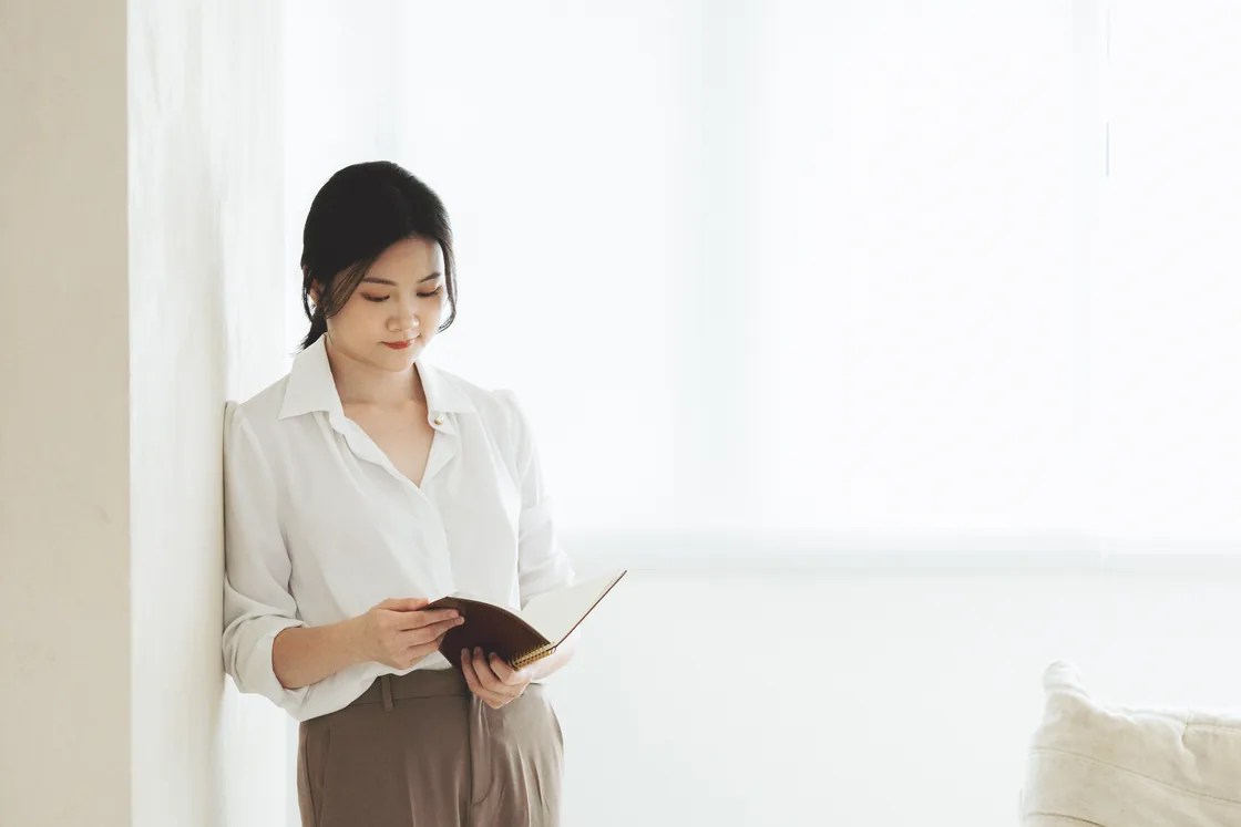 Lauren 穿著白襯衫，在窗邊閱讀筆記本